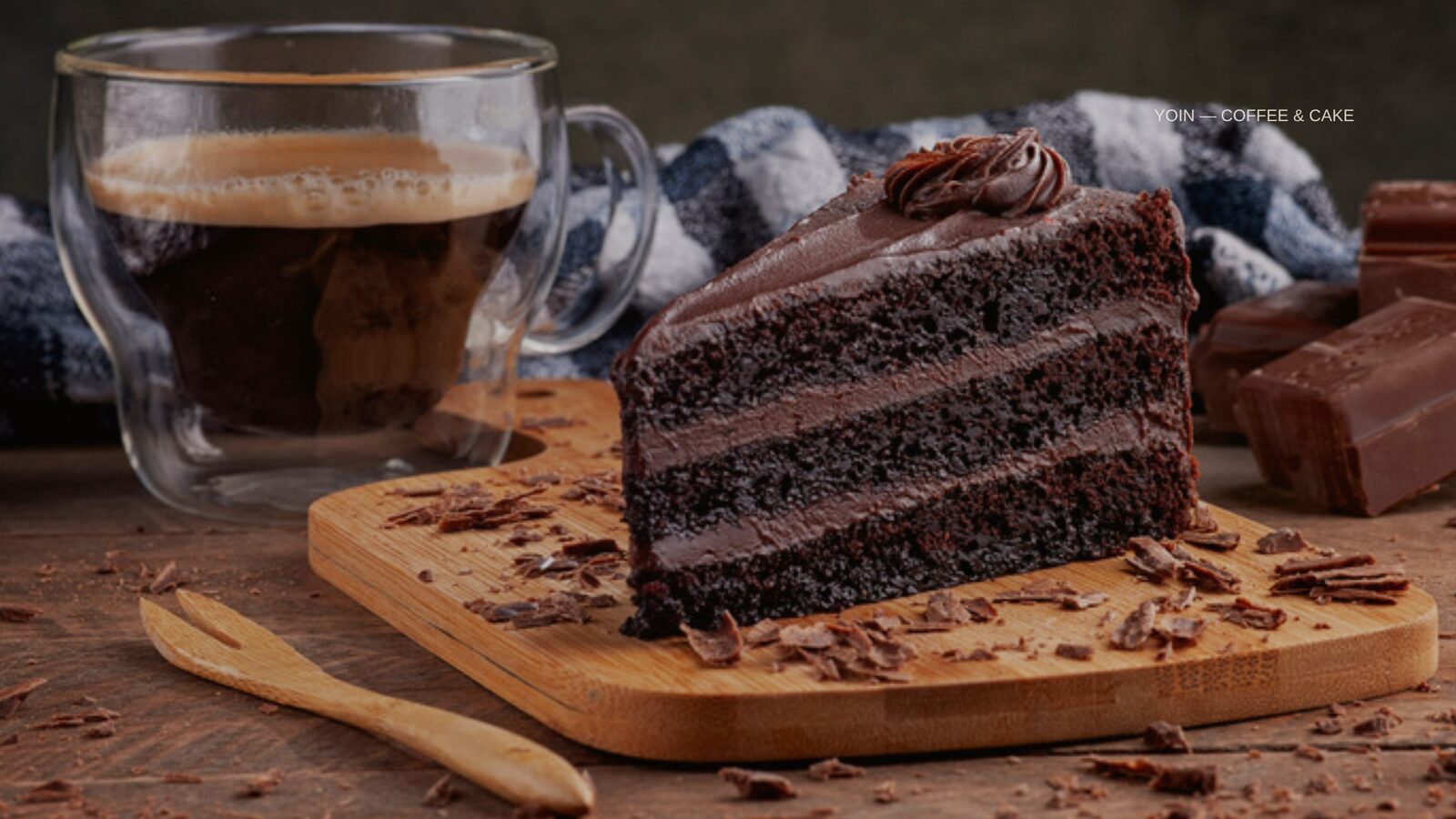 木のボードにのった三層のチョコレートケーキと、グラスのコーヒー